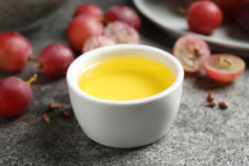 Bowl of natural grape seed oil on grey table. Organic cosmetic