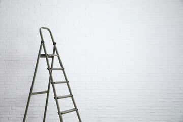 Metal stepladder near white brick wall. Space for text