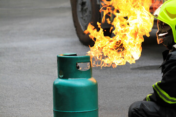 Fire burning on green gas container. and Firefighter or fireman in black uniform and wearing safety...