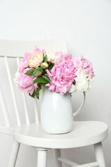 Beautiful fragrant peonies in jug on white chair
