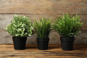 Artificial plants in black flower pots on wooden table