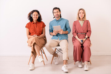 Obraz premium Two cute intercultural girls and young man with tablet sitting on chairs