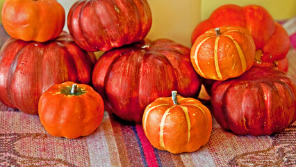 This centerpiece decor is a stack of varied colored pumpkins on a textured table runner against a green colored wall.  Perfect for autumn and Thanksgiving decor.