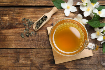 Cup of tea and fresh jasmine flowers on wooden table, flat lay. Space for text