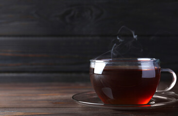 Cup of tasty black tea on wooden table. Space for text
