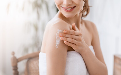 Young woman wrapped in towel applying lotion on shoulder
