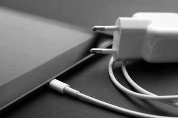 Tablet and charger on black background, closeup. Modern technology