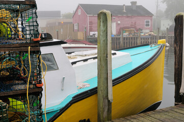 Fototapeta na wymiar Lobster traps with yellow boat and red house in fog at Fishermans Cove Eastern Passage Halifax Nova Scotia