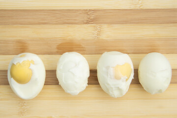 Four cooked and peeled chicken eggs lie on a cutting board on a wooden background. You can see the...