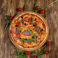 Italian pizza with ham, tomatoes, olives and basil on wooden table. Top view with copy space