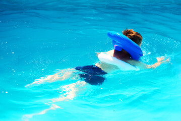 A little boy swims in the pool in an inflatable vest. The concept of sport and healthy lifestyle.