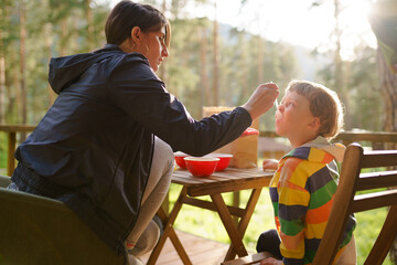 Mother feeds her son on the camping terrace