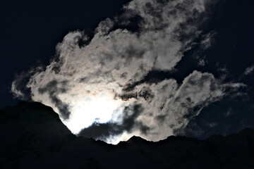 Artistic impressive dark cloud picture with the sun shining through clouds over mountains