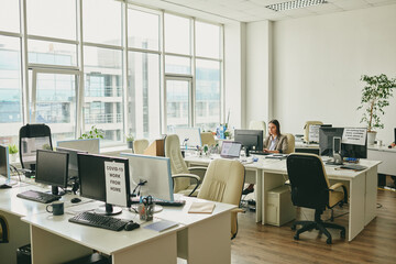 Young elegant businesswoman sitting by desk in the corner of modern office