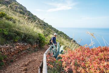 Peaceful view with red flowers and sea in Nature Reserve Zingaro in Sicily. Traveller on the path.