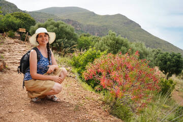 Smiling woman. Peaceful view with red flowers in Nature Reserve Zingaro in Sicily. Traveller on the path.