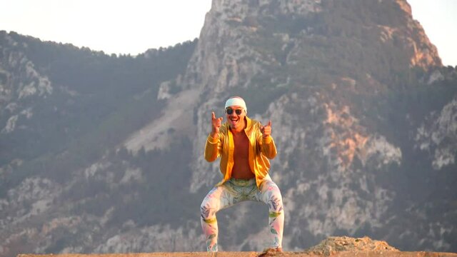 Young bald slender freak man in tight leggings, gold jacket, bandage on his head, dancing on roof, abnormal crazy, jumping, grimacing, showing ass, teasing. Slow motion video. Humor, unusual people
