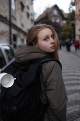 Fototapeta na wymiar A young girl in the background of the city, with a backpack behind her, a white hiking cup on a harness portfolio, travel, tourism