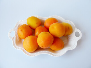 lots of ripe apricots on a plate on a light background