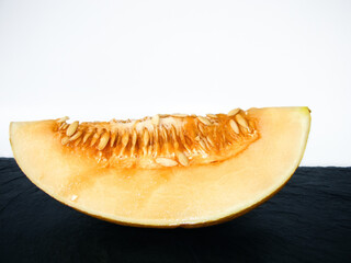 A piece of ripe melon with seeds on a stone tray. Side view.