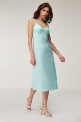 Woman beautiful face natural make up brunette hair tanned skin body wear fashion summer collection organic cotton long light blue skinny dress style for romantic date walk, accessory shoes sandals.