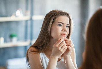 Skin problem. Young woman squeezing her pimple in front of mirror in bathroom