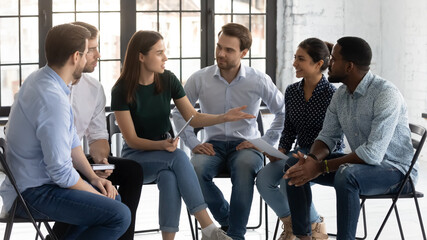 Six diverse mates sit together on chairs taking part in seminar, negotiations preparations, build...