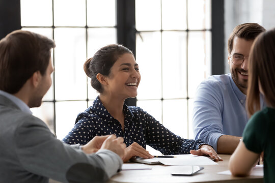 Diverse office workers gathered in boardroom morning briefing having pleasant informal chat laughing enjoy friendly atmosphere warm relations between colleagues, telling jokes after corporate meeting