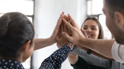 Close up stacked palms of diverse business people gathered together in office celebrating...