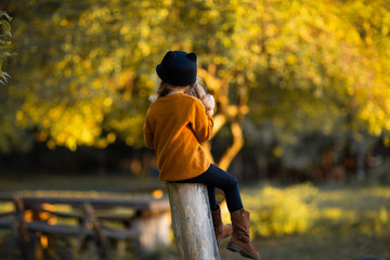 Little girl in red autumn clothes sitting by her back at the wooden fence. Copy space.