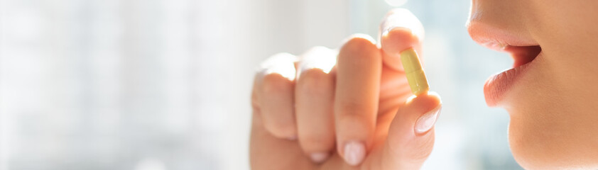 a woman takes a capsules. the girl brings the yellow capsule to her mouth