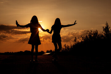 Two blond teenage girls ride skateboards at beautiful sunset.