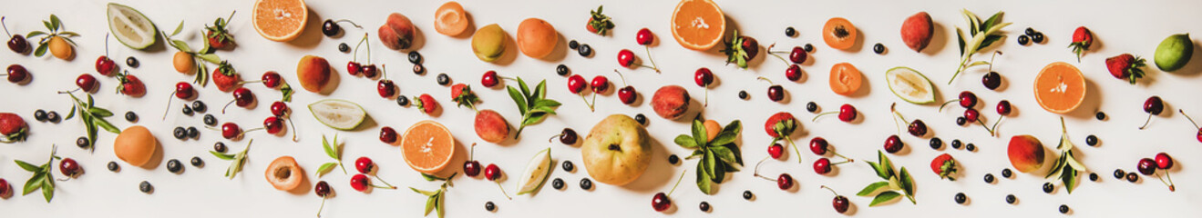 Fresh summer fruit and berries variety layout. Flay-lay of peaches, apricots, cherries, strawberries, blueberries, oranges and limes over plain white background, top view, wide composition