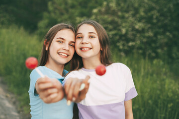 Two happy teenage girls holding a bright red lollipop candy.