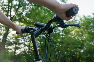 Fototapeta na wymiar close up image of child's hands hold black handlebar of bike while riding bicycle on countryside road in green forest. Happy summer vacation concept.