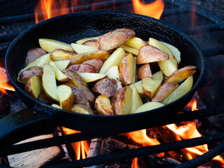Cooking fried potatoes in a pan on a wire rack on a fire