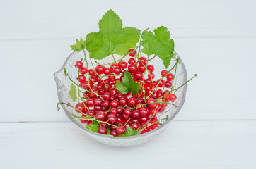 Fresh redcurrant berries in a glass bowl on a white wooden background