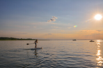 Young boy on the lake is rowing on the inflatable sup towards the sunset