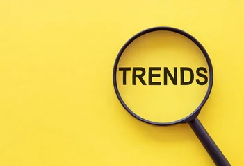 Fotobehang TRENDS text written on magnifier glasses, on yellow background. Main trend of changing something. Popular and relevant topics. New trends in business. Recent and latest trend. Evaluation methods. © Nastassia