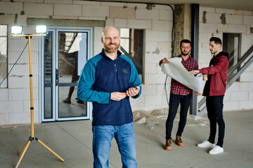 Young bald architect or contractor looking at you on background of colleagues