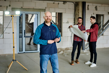 Fototapeta premium Young bald architect or contractor looking at you on background of colleagues