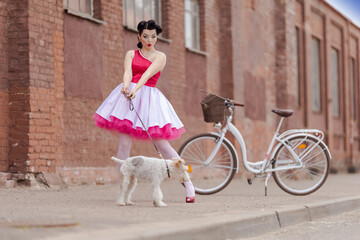 A girl in a dress and hairstyle in the style of the 40-50s on the city street with a dog breed Fox...