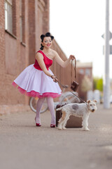 A girl in a dress and hairstyle in the style of the 40-50s on the city street with a dog breed Fox...