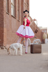 A girl in a dress and hairstyle in the style of the 40-50s on the city street with a dog breed Fox...