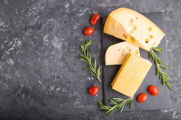 Various types of cheese with rosemary and tomatoes on black slate board on a black concrete...