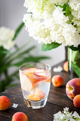 Refreshing drink with apricots and peaches, cold sparkling water with fruits, a vase of flowers viburnum opulus Roseum and a glass with a drink