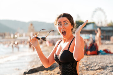 Portrait of a woman holds sunglasses and screams from sunburn. Redness on the skin of the face and...