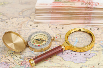 A compass with a bundle of big money and a magnifying glass are on the map