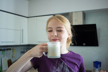 beautiful lady housewife with eyes closed standing in her white kitchen and enjoys strong coffee...