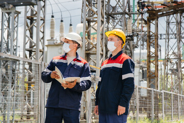 Engineers electrical substations conduct a survey of modern high-voltage equipment in the mask at the time of pandemia. Energy. Industry